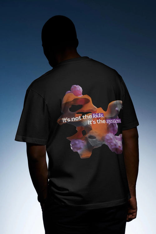 Black oversized T-shirt, back view on model, abstract graphic print with statement 'It's not the kids. It's the system.'